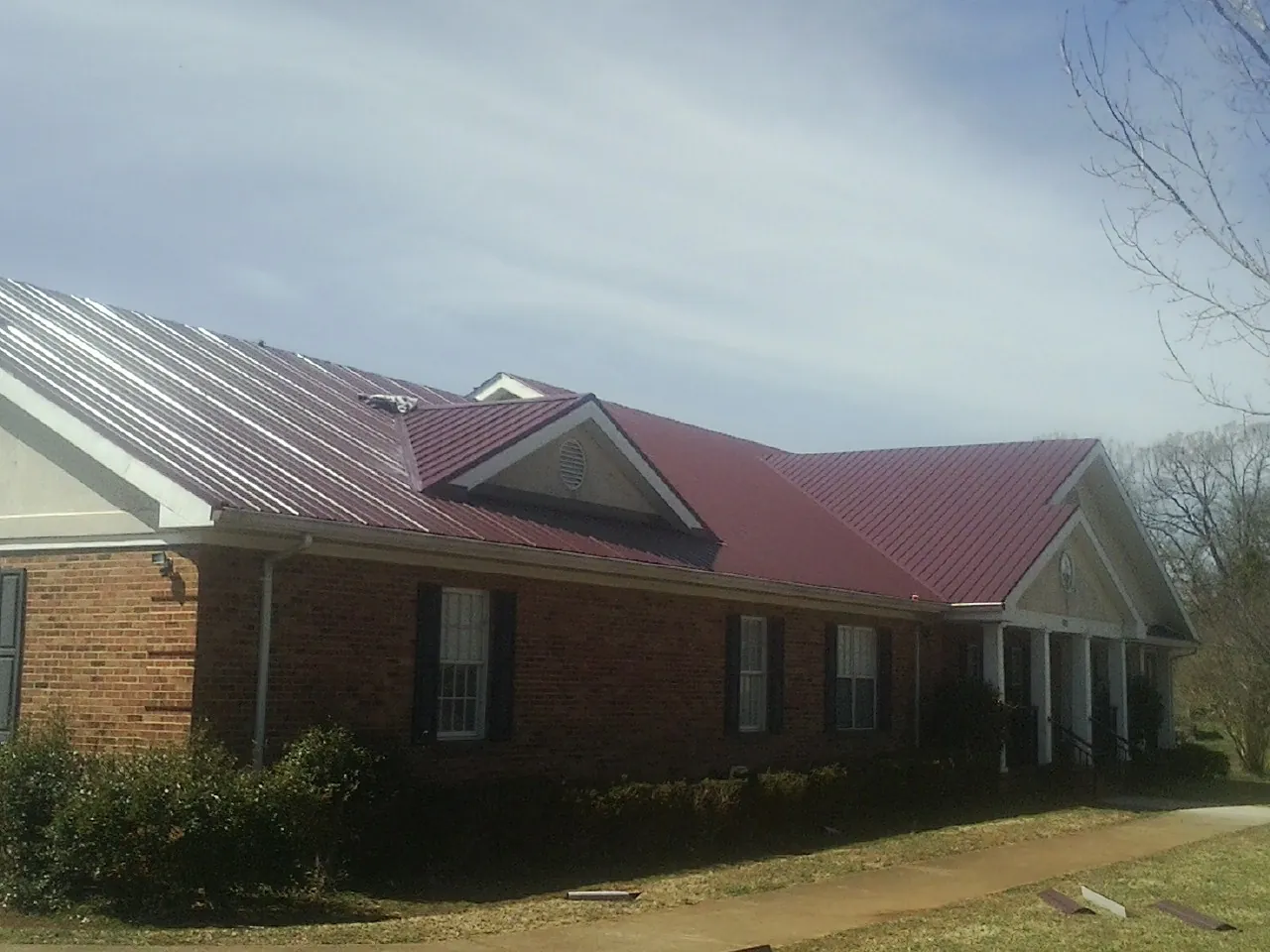 Red metal roof with gabled entries on a long brick building, from a Hail Damage Roof Repair job in Columbus